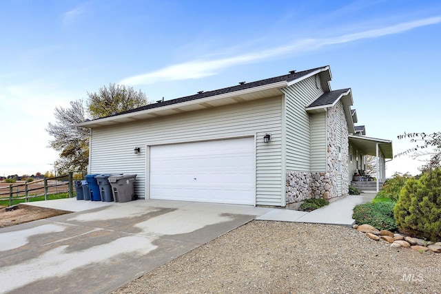 view of side of property with driveway, stone siding, a garage, and fence