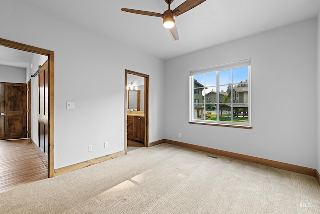 unfurnished bedroom featuring ceiling fan, a barn door, connected bathroom, and light hardwood / wood-style floors