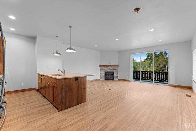 kitchen with light wood-type flooring, pendant lighting, sink, a fireplace, and kitchen peninsula