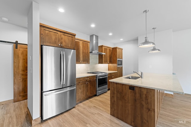 kitchen with wall chimney exhaust hood, a barn door, light hardwood / wood-style flooring, sink, and appliances with stainless steel finishes