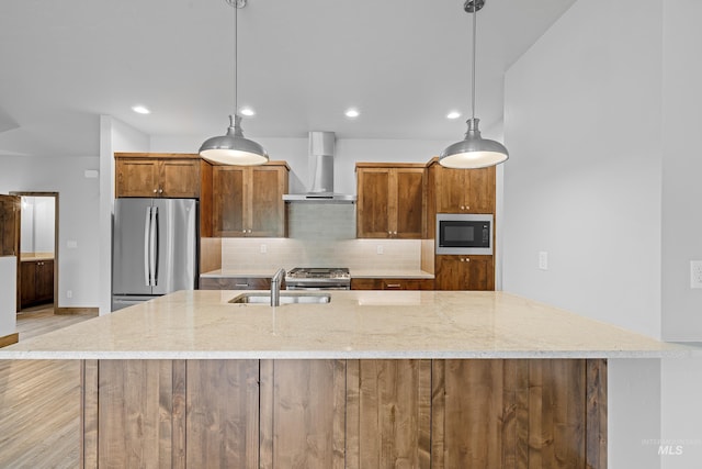 kitchen featuring appliances with stainless steel finishes, wall chimney range hood, decorative light fixtures, and sink