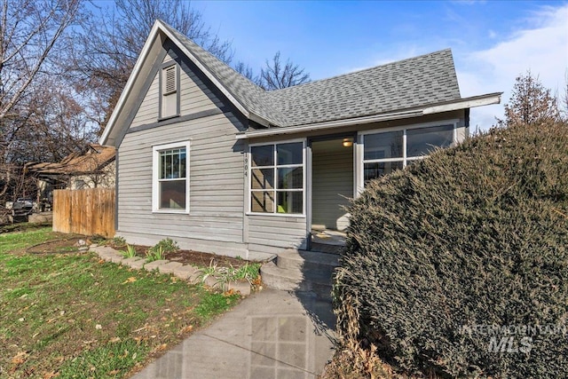 view of front facade featuring a shingled roof and fence