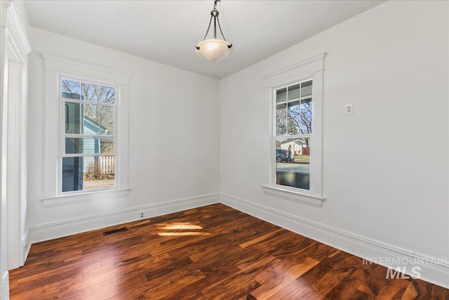 empty room with dark wood finished floors, baseboards, and visible vents