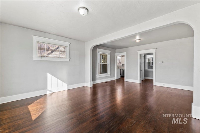 unfurnished living room featuring wood finished floors, arched walkways, and baseboards