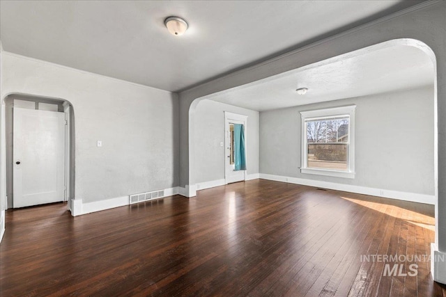 unfurnished room with arched walkways, visible vents, baseboards, and wood-type flooring