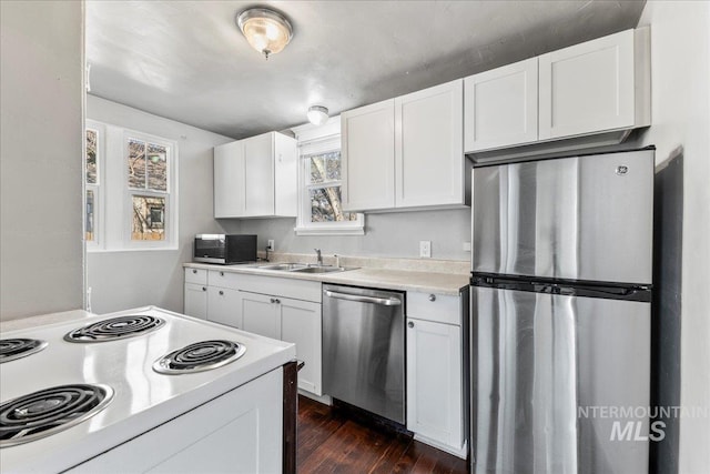 kitchen with dark wood-type flooring, light countertops, appliances with stainless steel finishes, white cabinets, and a sink