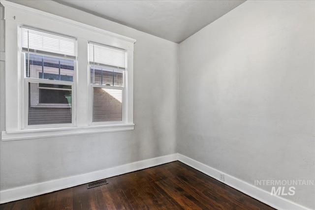 unfurnished room with baseboards, visible vents, and dark wood-style flooring