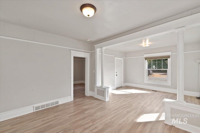 empty room featuring light wood-style floors, visible vents, ornate columns, and baseboards