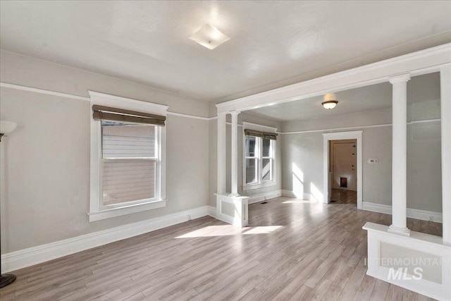 spare room featuring decorative columns, baseboards, and light wood-style flooring