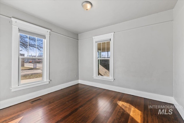 unfurnished room with dark wood finished floors, visible vents, and baseboards