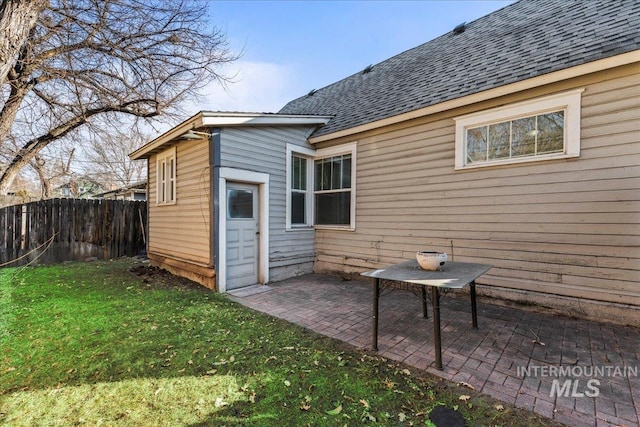 rear view of house featuring fence, a patio area, a lawn, and roof with shingles