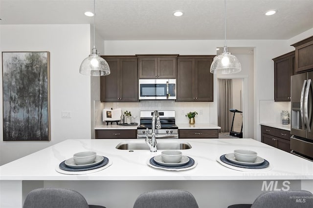 kitchen with a kitchen bar, stainless steel appliances, decorative light fixtures, and a kitchen island with sink