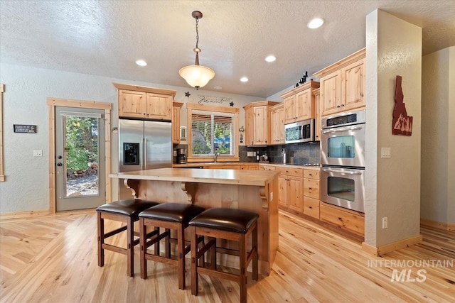23 Waterline Ln, Cascade, ID 83611 - kitchen featuring stainless steel appliances, light brown cabinetry, light wood-style floors, decorative backsplash, and healthy amount of natural light