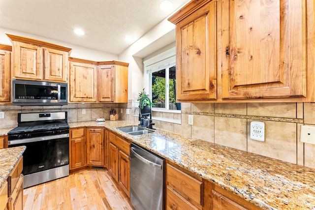 kitchen with light stone counters, light wood-style flooring, stainless steel appliances, a sink, and decorative backsplash