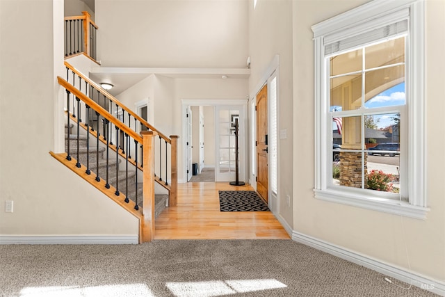 carpeted foyer with stairs, a high ceiling, and baseboards