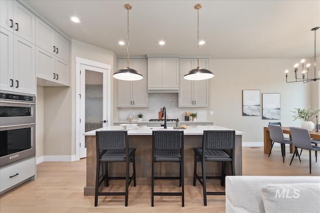 11966 W Zamalek Ct, Kuna, ID 83634 - kitchen with stainless steel double oven, light countertops, a chandelier, light wood finished floors, and a kitchen island with sink