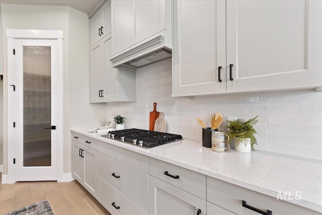 11966 W Zamalek Ct, Kuna, ID 83634 - kitchen with premium range hood, stainless steel gas stovetop, tasteful backsplash, light stone counters, and light wood-style floors