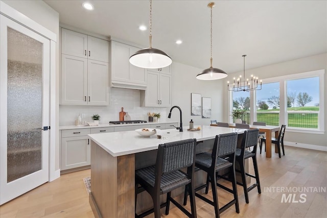 11966 W Zamalek Ct, Kuna, ID 83634 - kitchen with light countertops, a center island with sink, light wood-style flooring, a breakfast bar, and decorative light fixtures