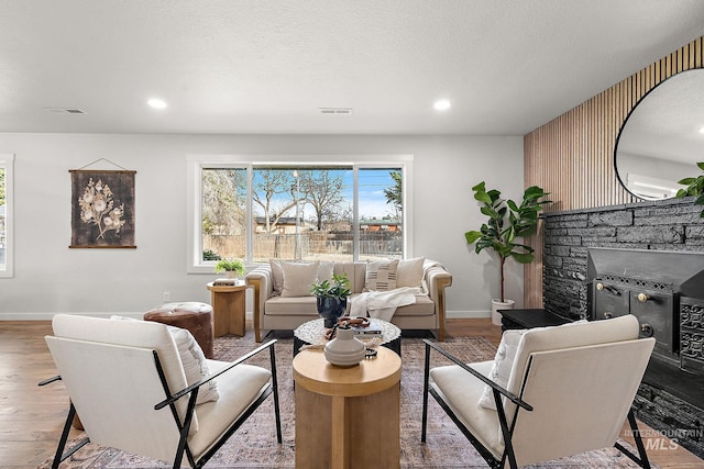 living room with baseboards, wood finished floors, recessed lighting, and a stone fireplace