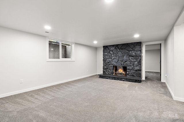 unfurnished living room featuring a stone fireplace, carpet floors, baseboards, and recessed lighting