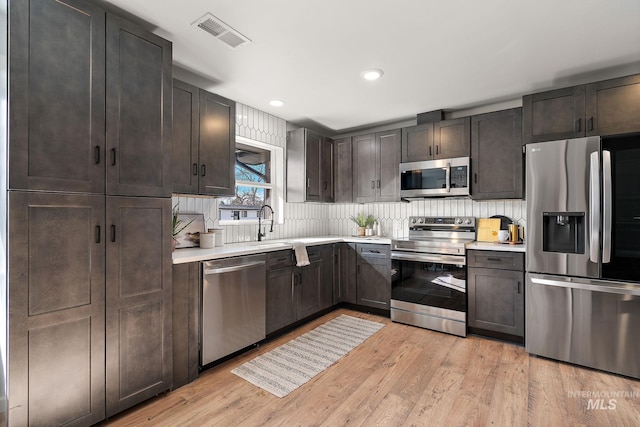 kitchen featuring stainless steel appliances, light countertops, a sink, light wood-type flooring, and recessed lighting