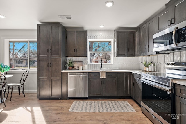 kitchen featuring stainless steel appliances, a sink, light wood-type flooring, dark brown cabinetry, and light countertops