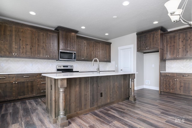 kitchen with dark hardwood / wood-style flooring, decorative backsplash, a kitchen island with sink, dark brown cabinets, and appliances with stainless steel finishes