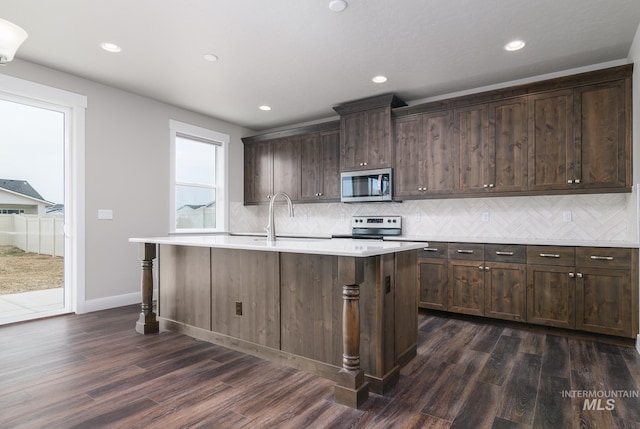 kitchen with dark wood-type flooring, a center island with sink, and appliances with stainless steel finishes