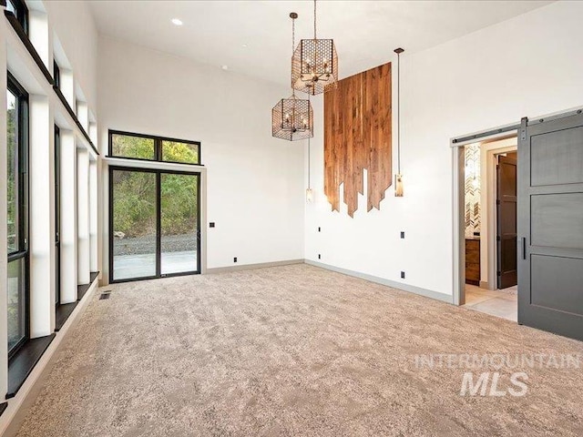 carpeted spare room with plenty of natural light, baseboards, a notable chandelier, and a high ceiling