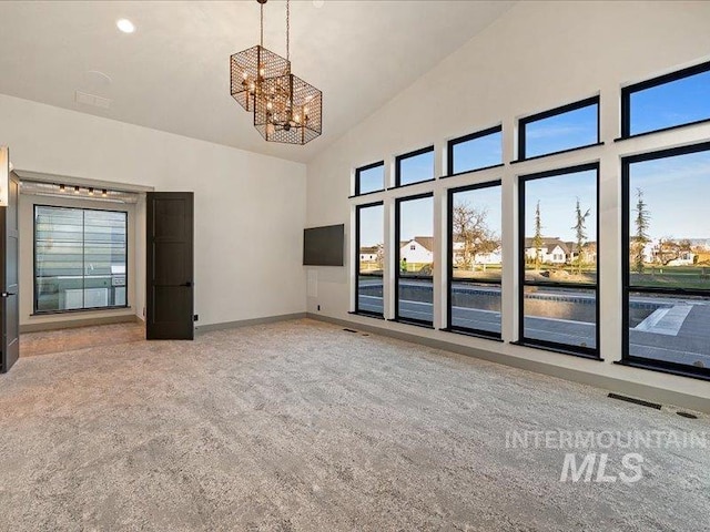 empty room with an inviting chandelier, carpet floors, high vaulted ceiling, and a wealth of natural light