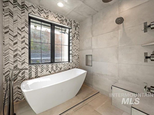 bathroom featuring a freestanding tub, tile patterned floors, and tile walls