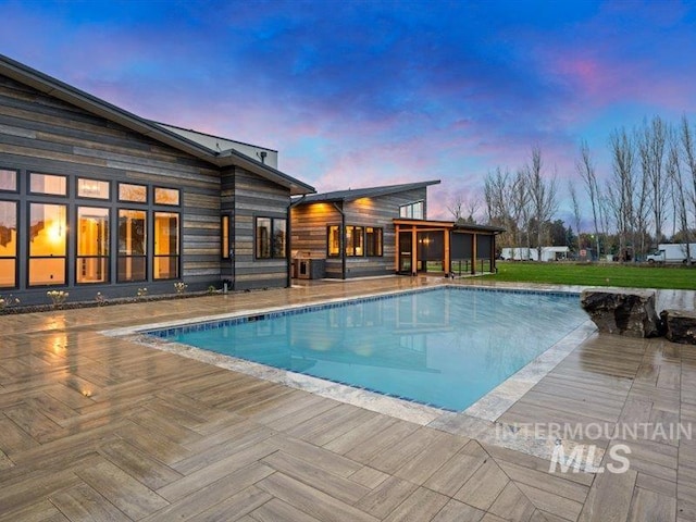 pool at dusk with a patio area, a yard, and an outdoor pool