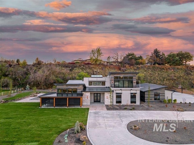 modern home with metal roof, a standing seam roof, curved driveway, and a front yard