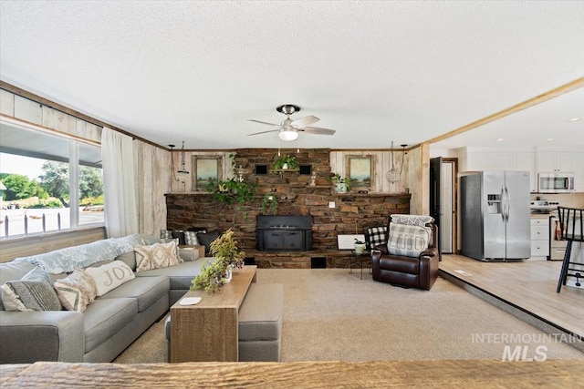 living room with a textured ceiling, light colored carpet, a wood stove, and a ceiling fan