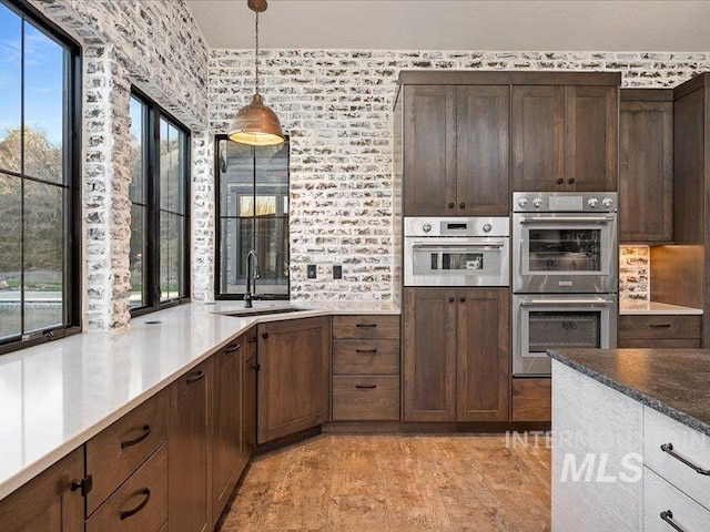 kitchen with double oven, hanging light fixtures, a sink, and dark brown cabinetry