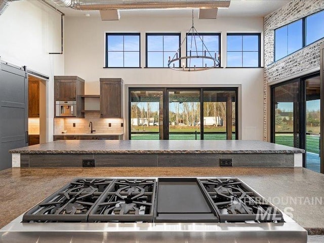 kitchen featuring decorative backsplash, a towering ceiling, dark countertops, and a notable chandelier