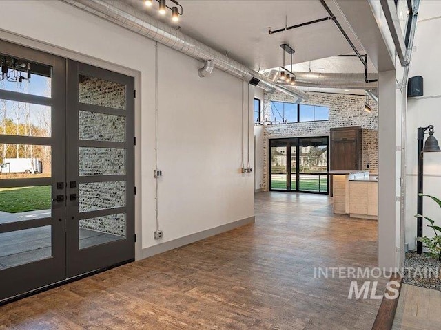 foyer entrance featuring french doors, baseboards, a high ceiling, brick wall, and wood finished floors