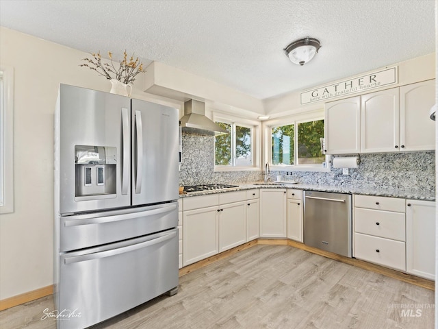 kitchen with light hardwood / wood-style flooring, white cabinetry, stainless steel appliances, decorative backsplash, and wall chimney exhaust hood