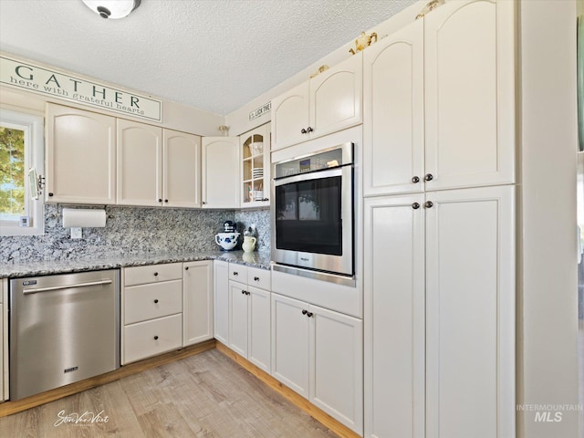 kitchen with light hardwood / wood-style flooring, stainless steel appliances, light stone countertops, a textured ceiling, and white cabinets