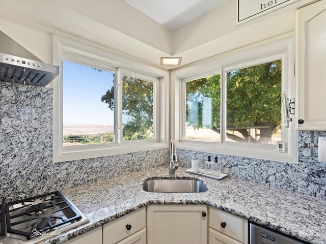 kitchen featuring white cabinetry, sink, gas stovetop, light stone countertops, and wall chimney range hood