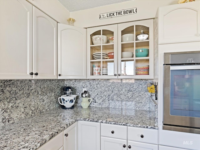 kitchen featuring light stone counters, stainless steel oven, a textured ceiling, and white cabinets