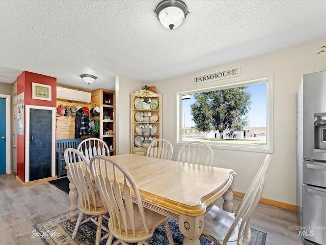 dining space with a wall mounted air conditioner, a textured ceiling, and light wood-type flooring