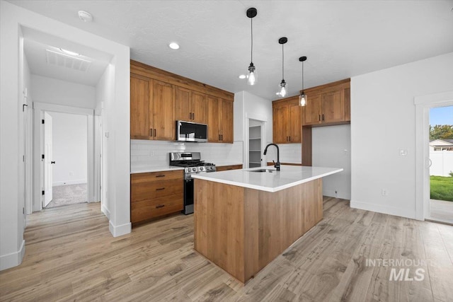 kitchen with stainless steel appliances, brown cabinets, a sink, backsplash, and light wood-style floors