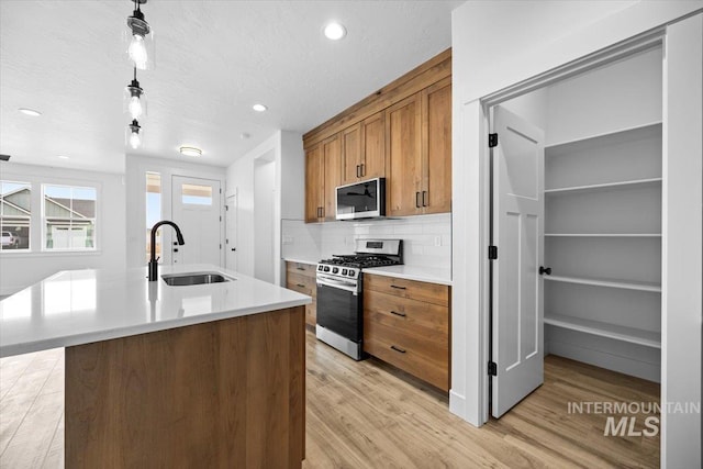 kitchen featuring stainless steel appliances, a sink, brown cabinetry, light wood-style flooring, and backsplash