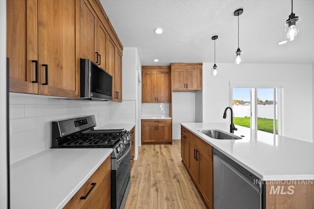 kitchen featuring stainless steel appliances, a sink, brown cabinets, light wood-style floors, and recessed lighting