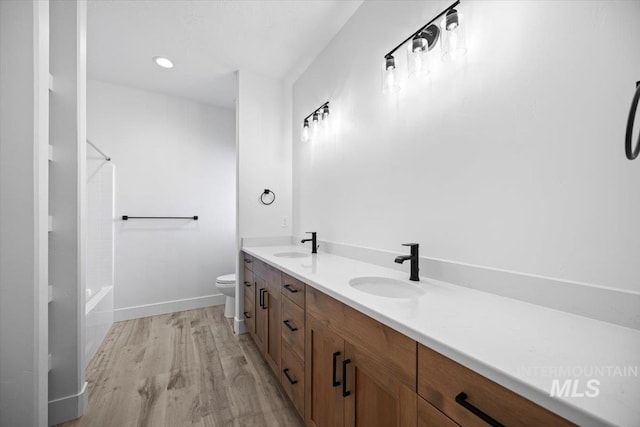 full bathroom with wood finished floors, toilet, double vanity, baseboards, and washtub / shower combination