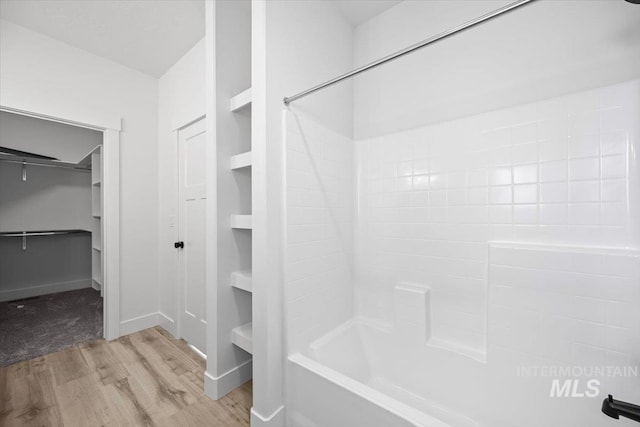 full bath featuring wood finished floors, a walk in closet, tub / shower combination, and baseboards