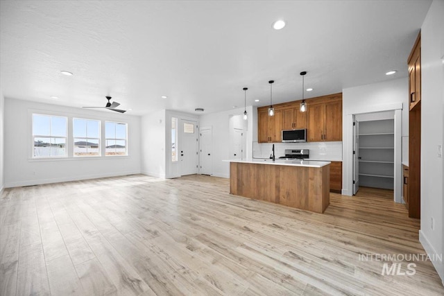 kitchen featuring stainless steel appliances, open floor plan, brown cabinetry, recessed lighting, and light countertops