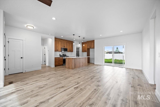 kitchen featuring stainless steel appliances, open floor plan, brown cabinets, light countertops, and light wood-type flooring