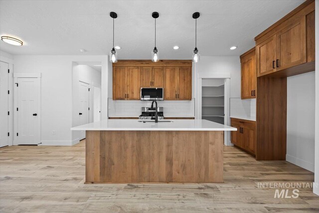 kitchen with stainless steel microwave, brown cabinetry, a sink, backsplash, and light wood-style floors